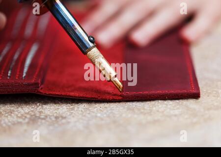 A leather craftsman works with leather. Sews leather goods. Making things handmade. Women's hands with a needle, thread, scissors and a blowtorch. Clo Stock Photo