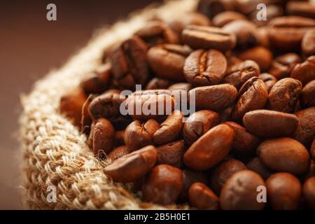 Coffee beans closeup in burlap bag on wooden background. Aromatic roasted coffee beans. The view from the top. Macro Stock Photo