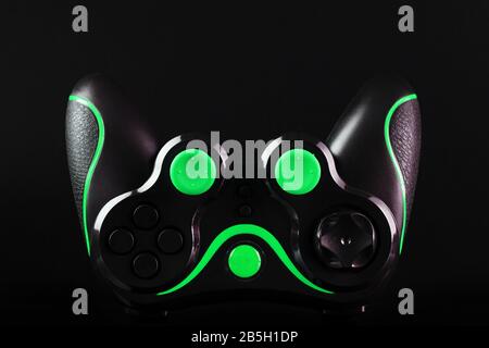 Black game controller gamepad with green buttons on black background upside down close up. Device to control and control the game. Video games on PC, Stock Photo