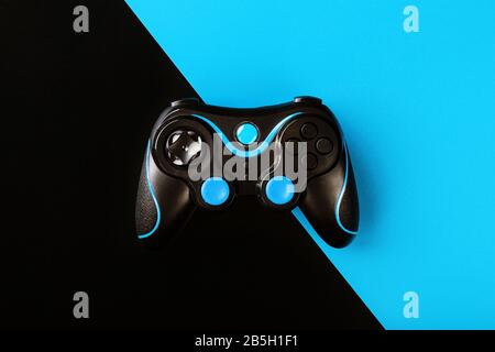 Black gamepad on black and blue background, by . Game concept. Device to control and control the game. Video games on PC, console, smartphone. Stock Photo
