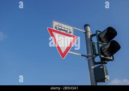 Low angle view of Caution and warning triangular sign with tram symbol and traffic light on column over light rail crossing against blue sky. Stock Photo