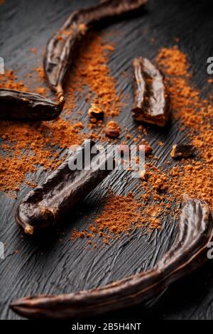 Carob carob fruit with powder on black background. Blast the Sweet powder from the pulp of the pods. Substitute cocoa and sugar, chocolate patients wi Stock Photo