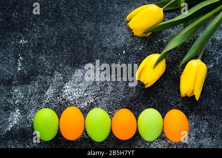 Paschal mockup with copy space. Festive easter frame with painted eggs and yellow tulips on black concrete background. Template, card with creative mo Stock Photo