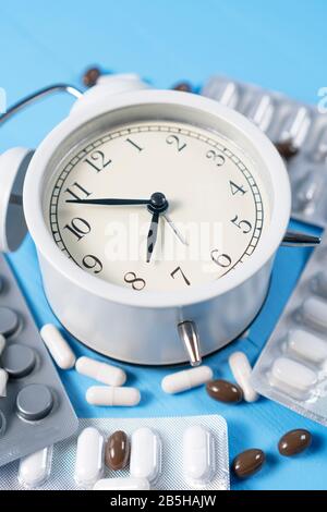 Analog alarm clock with blister packs of medical capsules on a light blue wooden background. Contraceptive concept Stock Photo