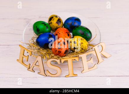 Multi-colored Easter quail eggs and the inscription Easter on a plate. Copy space. Stock Photo