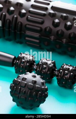 A set of black bumpy foam massage rollers, body rollers, rubber balls on a blue background for mechanical and reflex action on tissues and organs. Stock Photo