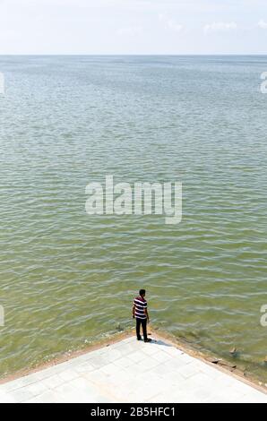 Single isolated boy standing and looking at the vast expanse of the submerged white desert in monsoon season, giving a sense of scale. Stock Photo