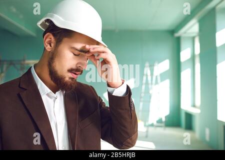 Builder foreman in a white helmet surprised in shock at a construction site indoors. Stock Photo