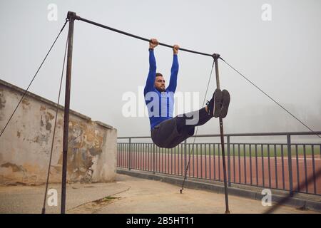 A bearded guy doing pull-ups on a horizontal bar in a stadium in the fog. Health. Healthy lifestyle. Stock Photo