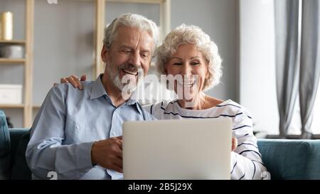 Overjoyed mature couple rest on sofa using laptop Stock Photo