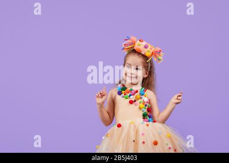 Childrens birthday party, masquerade. Little happy toddler child girl in a puffy tutu fancy dress, having fun on Violet background. Space for text Stock Photo