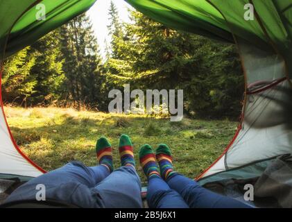 View from inside with couple of legs inside camping tent - Travel wanderlust concept with young people enjoying adventure experience.  Concept about t Stock Photo