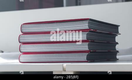 Stack of four thick new books on a white table Stock Photo