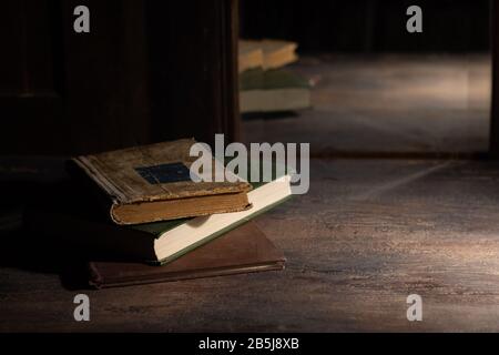 Three old books on a wooden table are reflected in an old mirror Stock Photo