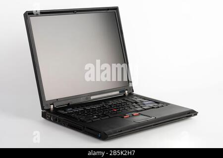 Old laptop on white background, which was produced in 2005, outer cover reinforced titanium, metal hinges, red trackpoint. Stock Photo