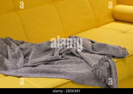 Modern yellow sofa with a gray plaid on it. Close up. Stock Photo