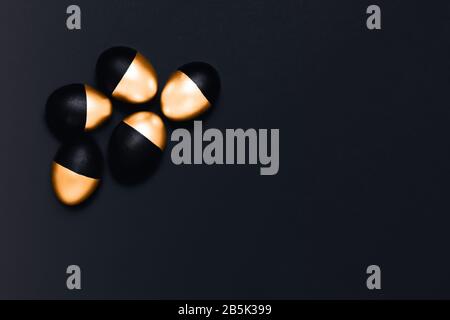 Five black and golden Easter eggs on dark grey background. Flat lay, top view, copy space. Stock Photo