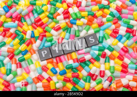 Mass of colourful pills / gelatine capsules & PILLS in letter tiles. For NHS, big pharma, Medicare, Medicaid, illness cured, Covid-19 cure bitter pill