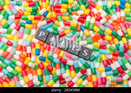 Mass of colourful pills / gelatine capsules & PILLS in letter tiles. For NHS, big pharma, Medicare, Medicaid, illness cured, Covid-19 cure bitter pill