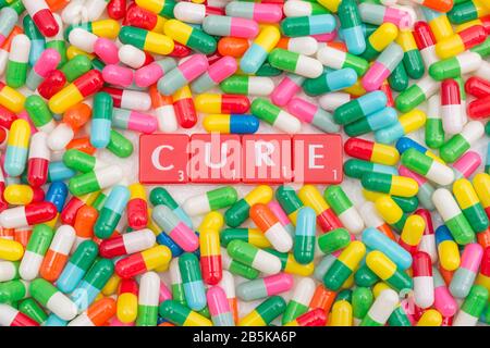 Mass of colourful pills / gelatine capsules & CURE in letter tiles. For NHS, big pharma, Medicare, Medicaid, illness cured, coronavirus cure, Covid-19 Stock Photo