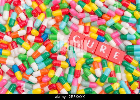 Mass of colourful pills / gelatine capsules & CURE in letter tiles. For NHS, big pharma, Medicare, Medicaid, illness cured, coronavirus cure, Covid-19