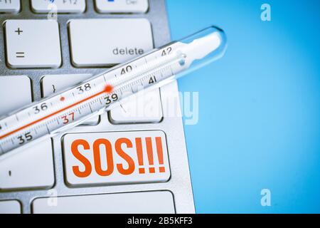 Thermometer on a keyboard with a button sos on a blue background. Close up. Stock Photo