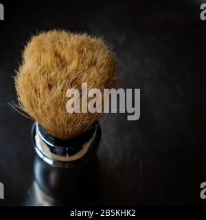 Shaving brush on the rustic black background, top view in chiroscuro style. Skin care for men. Place for text, square format. Stock Photo