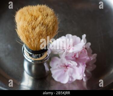 Shaving brush with geranium flowers of tender pink color on a aged steel vase, top view in chiroscuro style. Skin care for men. Place for text, square Stock Photo