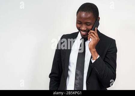 Portrait of african man smiling while talking on the phone with grey wall on background with copy space Stock Photo