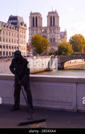 Live statue street artist sweeping on bridge with Notre Dame Cathedral in background, Paris Stock Photo