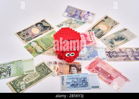 Assembled red lego piggy bank surrounded by different currencies paper notes from around the world Stock Photo