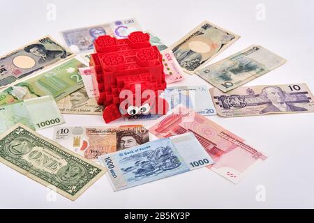 Assembled red lego piggy bank surrounded by different currencies paper notes from around the world Stock Photo