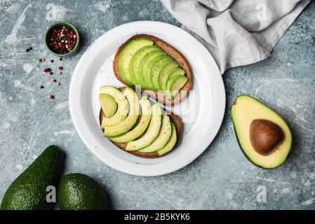 Rye bread toast with sliced avocado on plate, table top view. Healthy vegan vegetarian plant based food Stock Photo