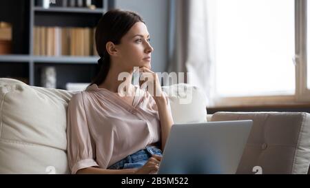 Distracted from work young woman sitting on couch with laptop. Stock Photo