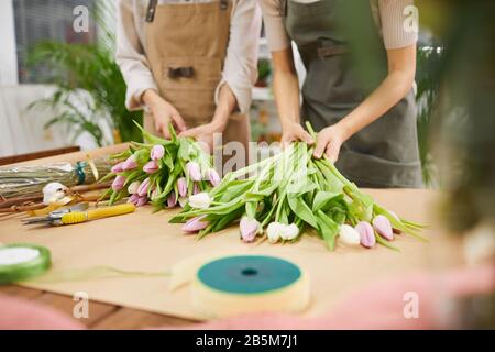 Cropped portrait of two young women arranging floral compositions and tulip bouquets for Spring season while working in flower shop, copy space Stock Photo