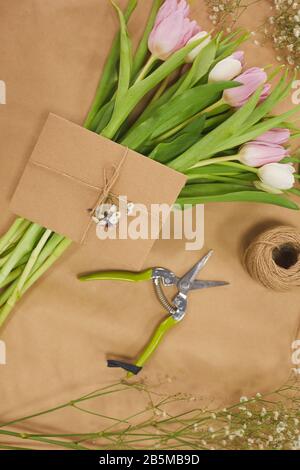 Top view at Spring theme composition with pastel pink tulips on wooden table and craft envelope or greetings card flower shop background Stock Photo