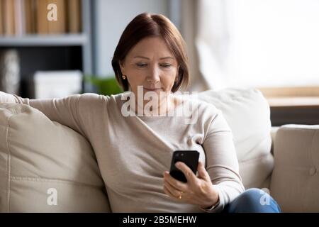 Worried middle aged woman looking at mobile phone screen. Stock Photo