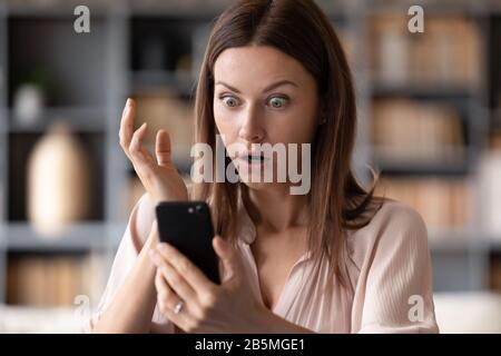 Close up young shocked woman looking at mobile phone screen. Stock Photo