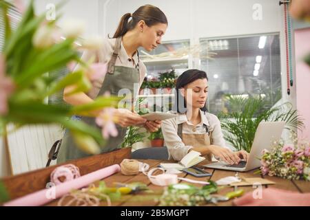 Side view portrait of two young businesswomen using laptop while managing flower shop, copy space Stock Photo