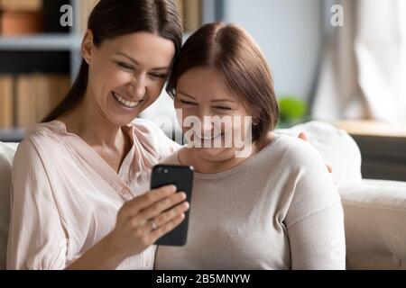 Happy young woman showing funny video to mature mother. Stock Photo