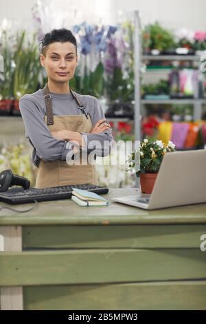 Waist up portrait of successful female business owner posing confidently with arms crossed while standing behind counter in flower shop, copy space Stock Photo