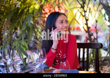 A young Vietnamese woman wearing a traditional red Ao Dai dress using her mobile phone Stock Photo
