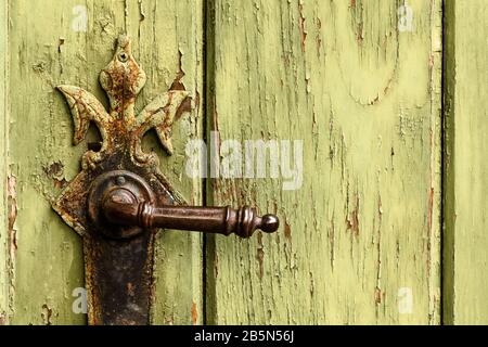 Old rusty door handle on green door. Detail of rustic old vintage and rusty grungy iron door handle installed on an ornamented old heavy and massive m Stock Photo
