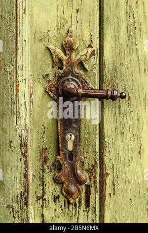 Old rusty door handle on green door. Detail of rustic old vintage and rusty grungy iron door handle installed on an ornamented old heavy and massive m Stock Photo
