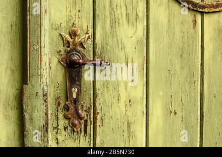 Old rusty door handle on green door. Detail of rustic old vintage and rusty grungy iron door handle installed on an ornamented old heavy and massive m Stock Photo