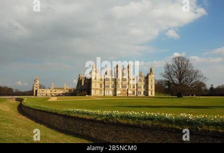 The west elevation of Burghley House set of by the Capability Brown lawn and daffodils Stock Photo