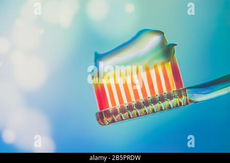 Orange plastic toothbrush with a toothpaste on a blue background. Side view. Art bokeh with copy space. Stock Photo