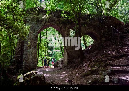 Two women hikers walk on the path under an old arch in valle delle ferriere nature reserve on the Amalfi Coast, Italy. Summertime. Summer’s day outing Stock Photo