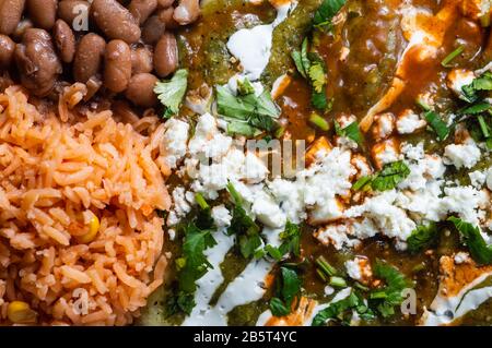 Enchiladas Verdes, or green enchiladas, tortillas filled with chicken and served with beans and Mexican style rice Stock Photo