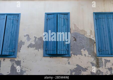 Three blue windows with shutters on a shabby wall Stock Photo